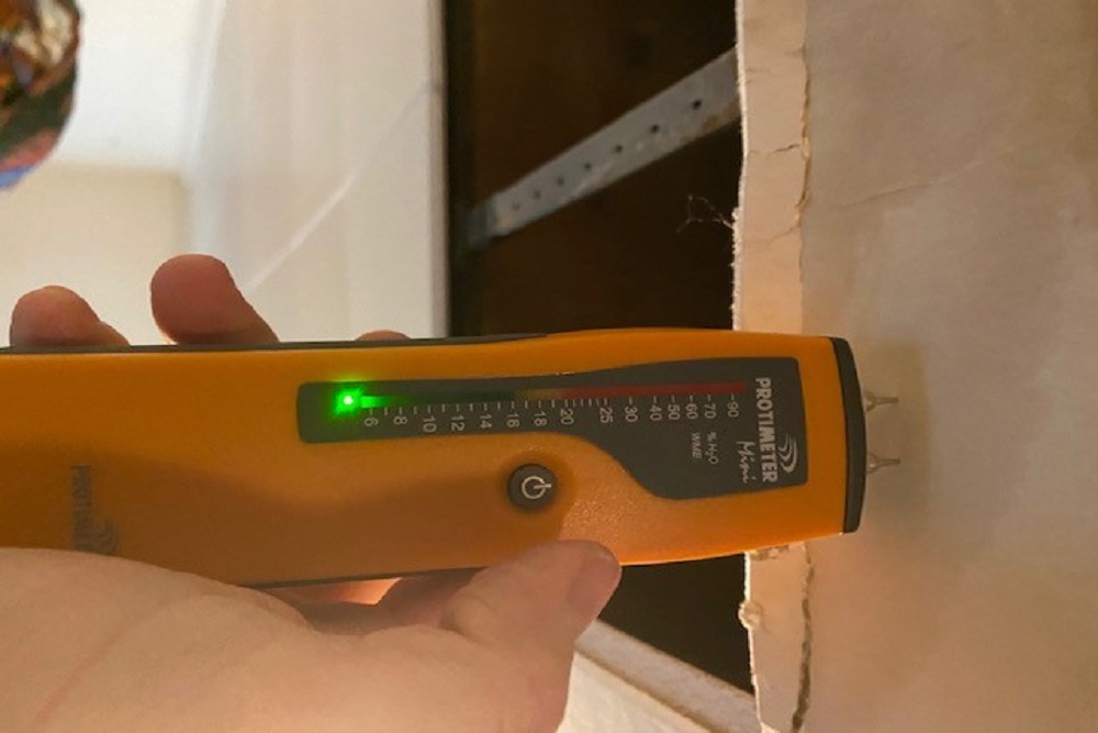 Hand holding a moisture meter up to a wall while providing home inspection services